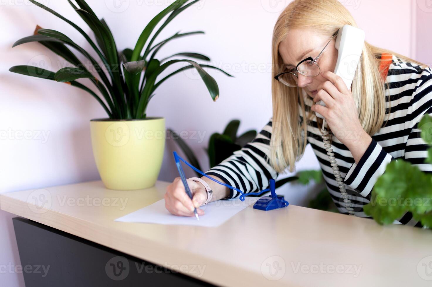 emotional middle-aged blonde woman talking on a landline at her workplace or office photo