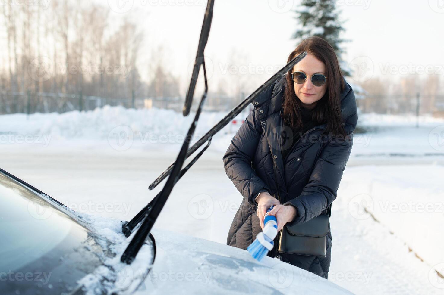 Woman cleans car with a brush from snow after a blizzar photo
