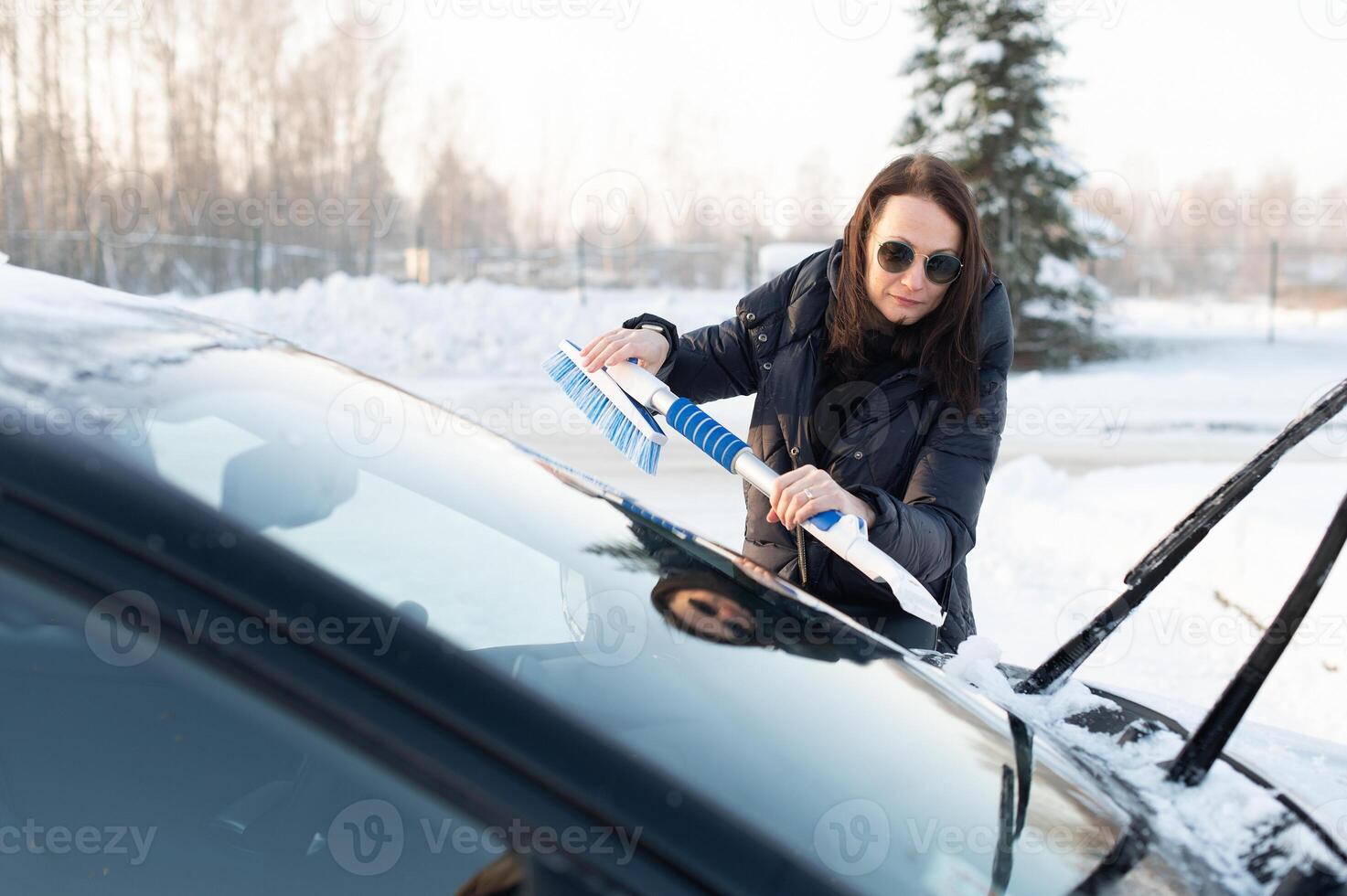 Woman cleans car with a brush from snow after a blizzar photo