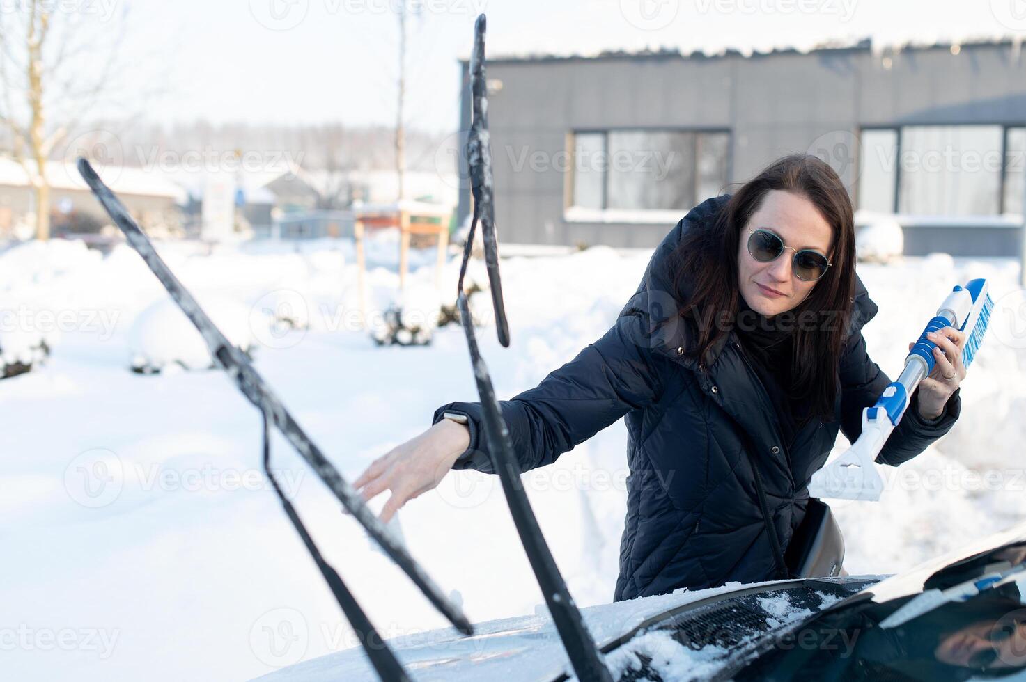Woman cleans car with a brush from snow after a blizzar photo