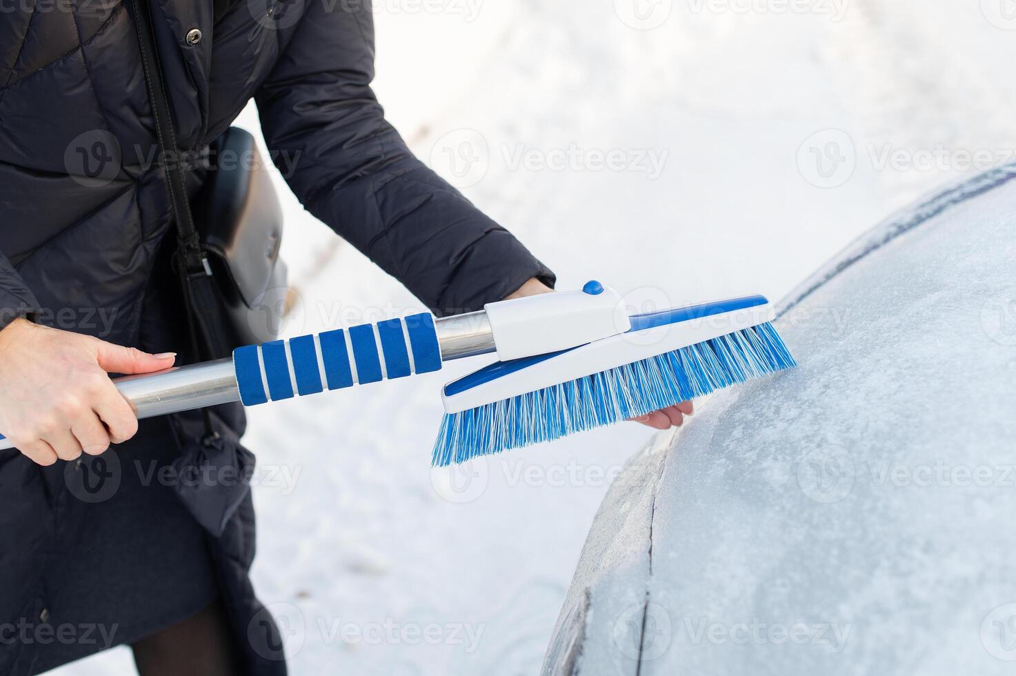 Woman cleans car with a brush from snow after a blizzar photo