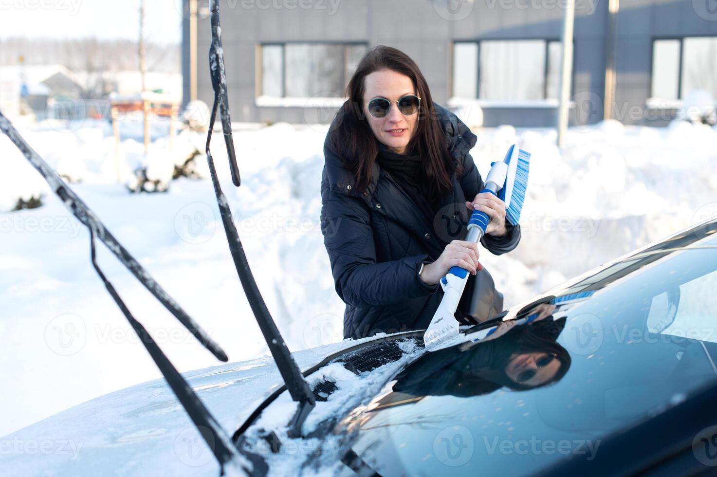 Woman cleans car with a brush from snow after a blizzar photo