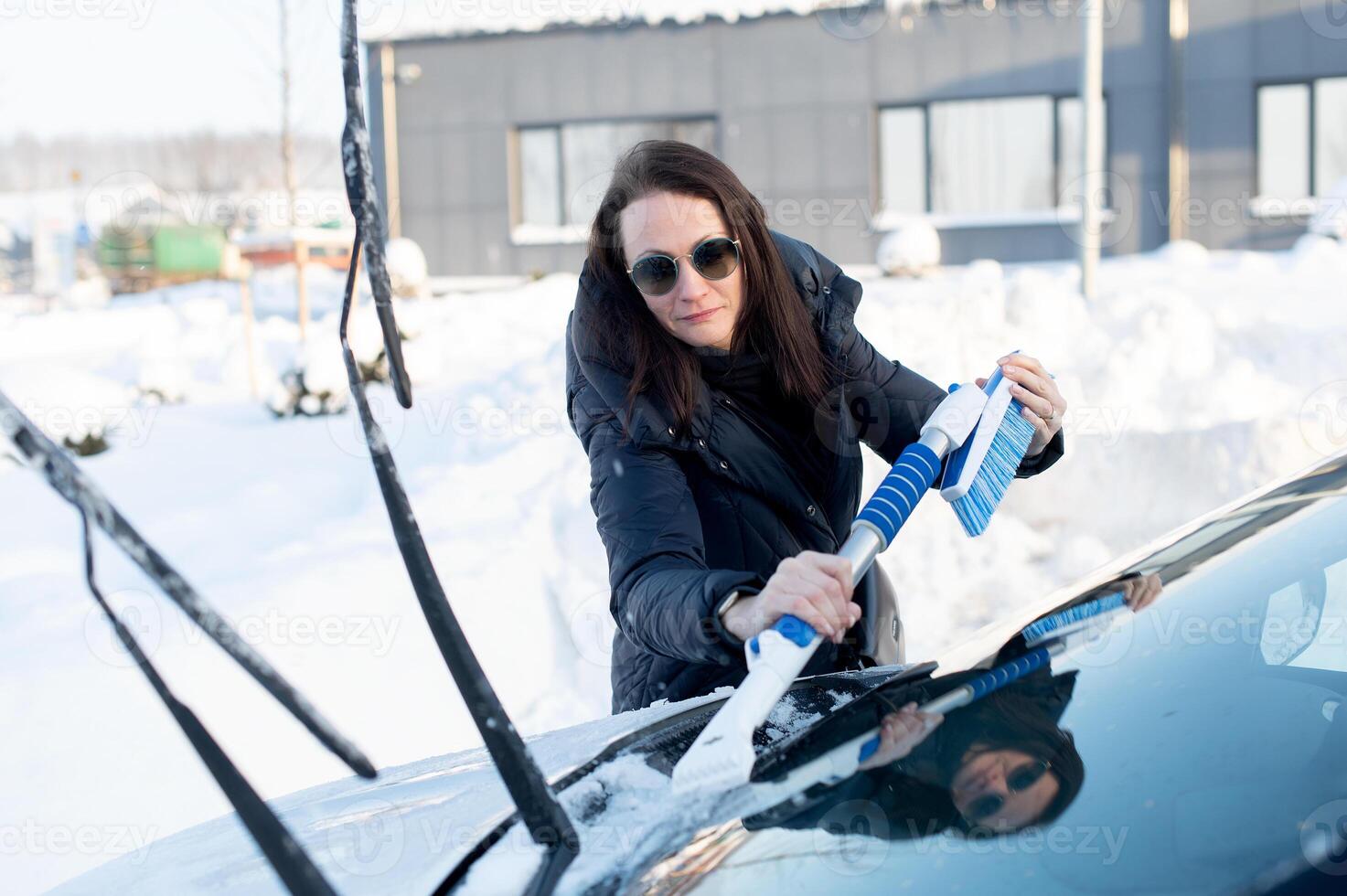 Woman cleans car with a brush from snow after a blizzar photo
