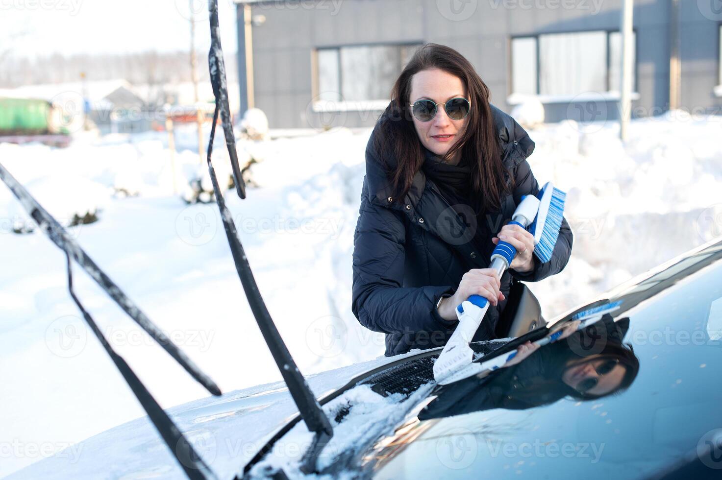 Woman cleans car with a brush from snow after a blizzar photo