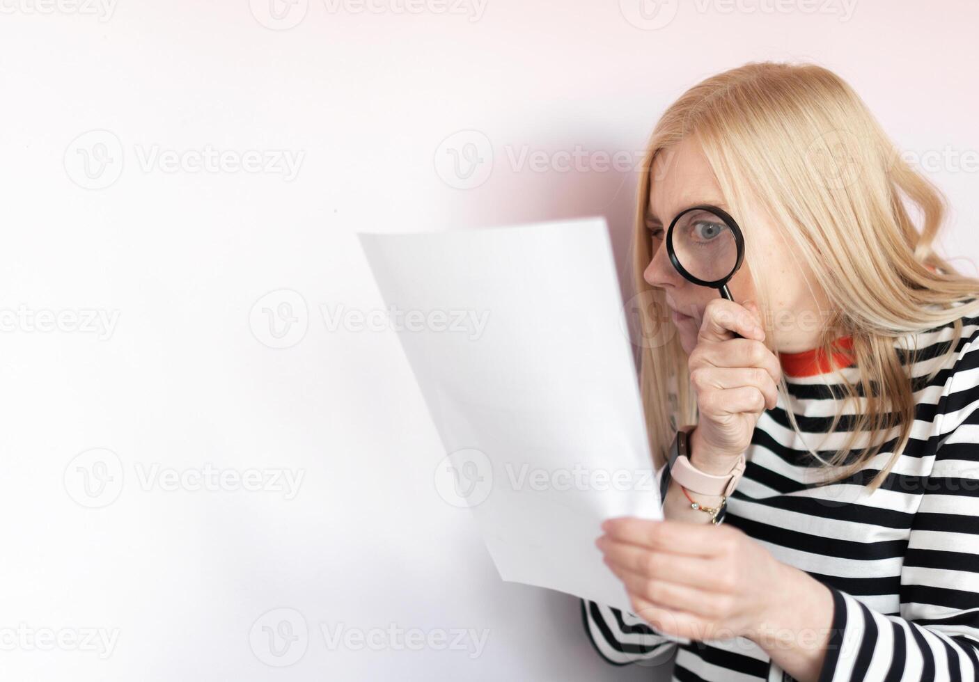 Middle aged funny woman with magnifying glass reading document on gray wall background isolated photo