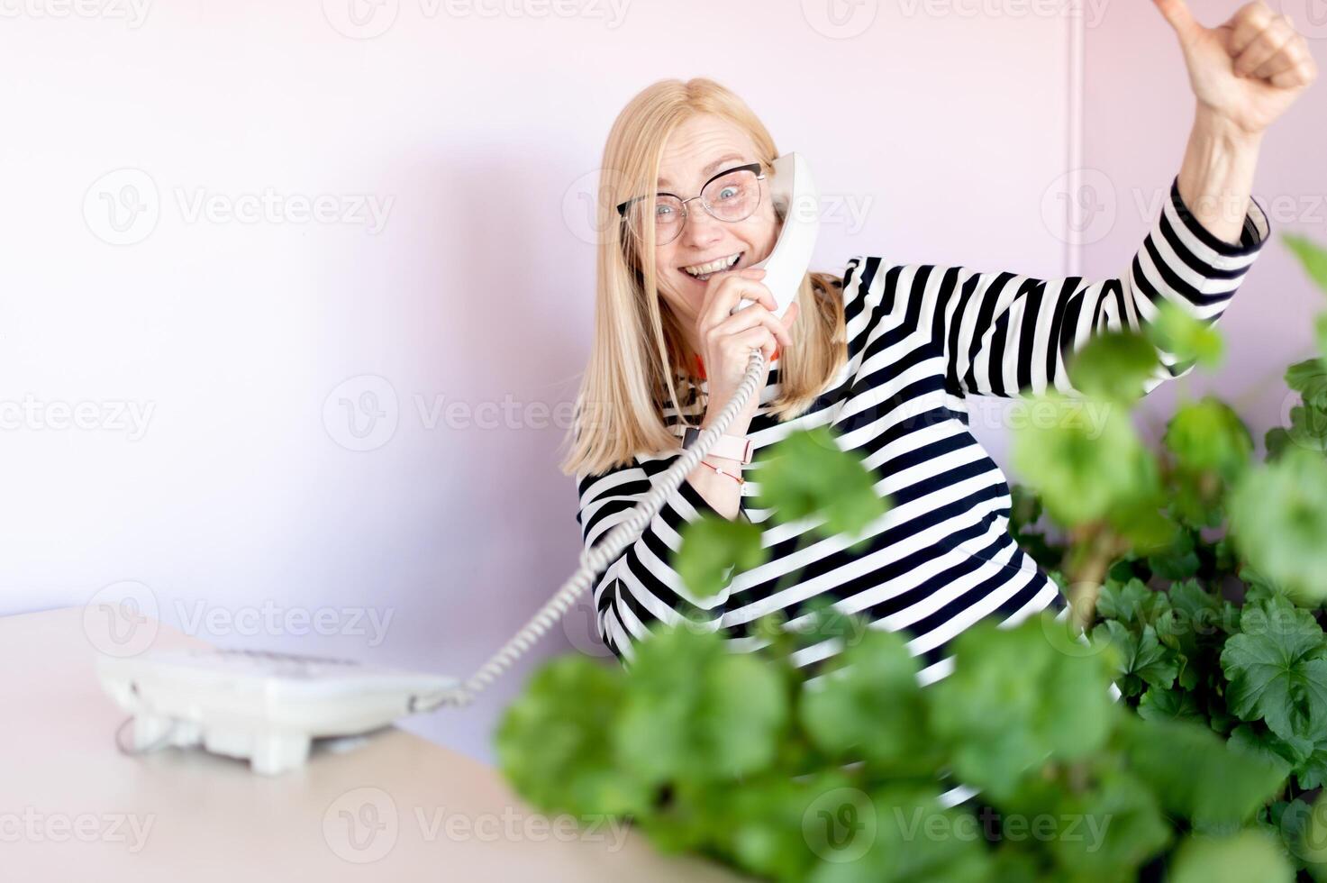 emotional middle-aged blonde woman talking on a landline at her workplace or office photo