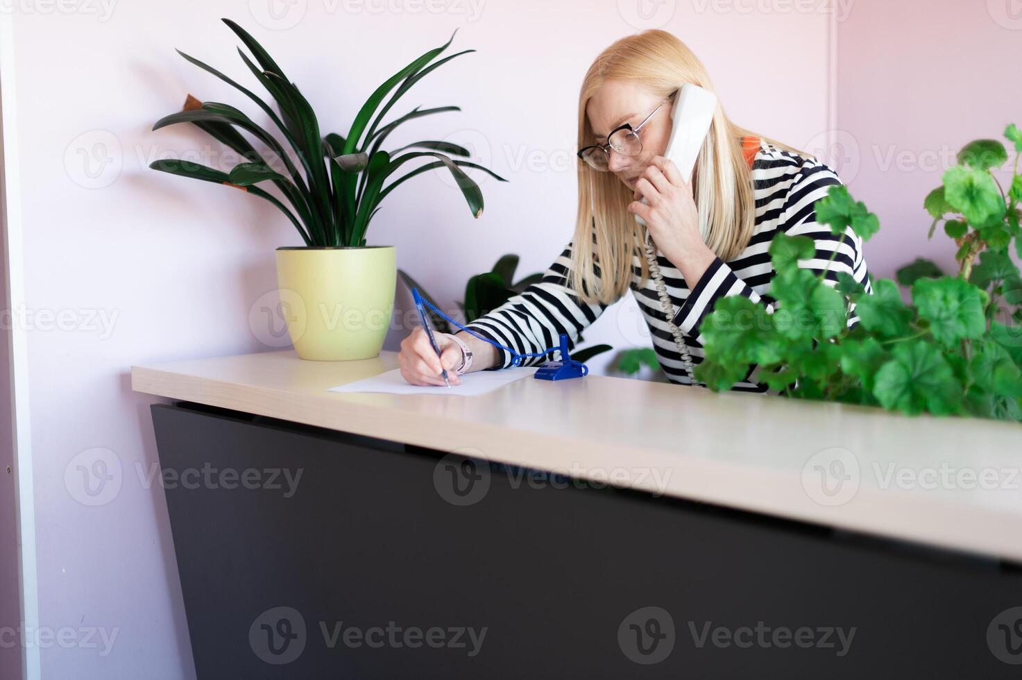 emotional middle-aged blonde woman talking on a landline at her workplace or office photo