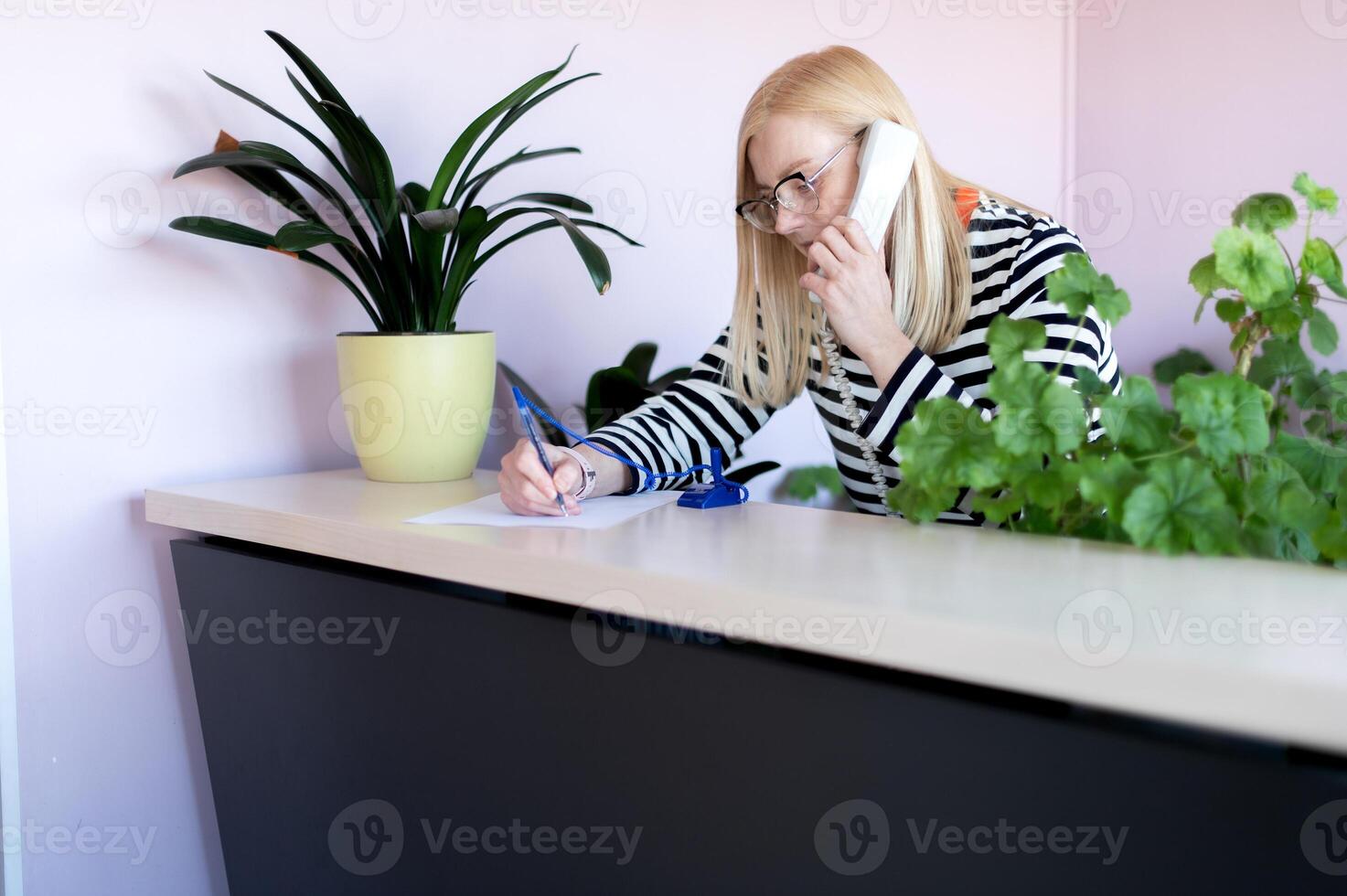 emotional middle-aged blonde woman talking on a landline at her workplace or office photo