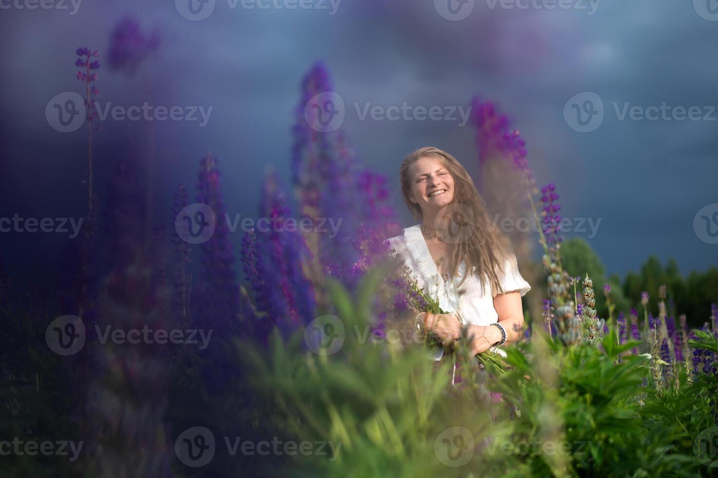 Young woman with lupine flowers under dark blue sky rain cloud background.Female holding bouquet photo