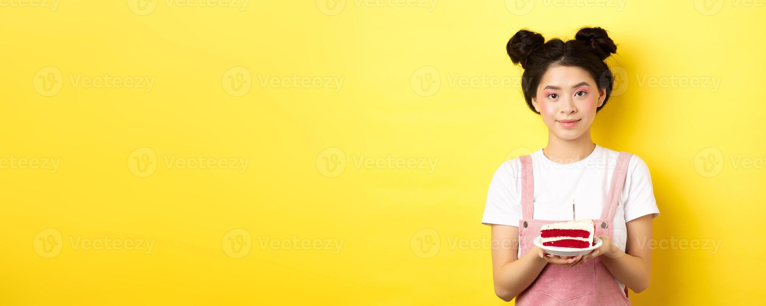 Asian birthday girl standing with cake and smiling, celebrating b-day on yellow background photo