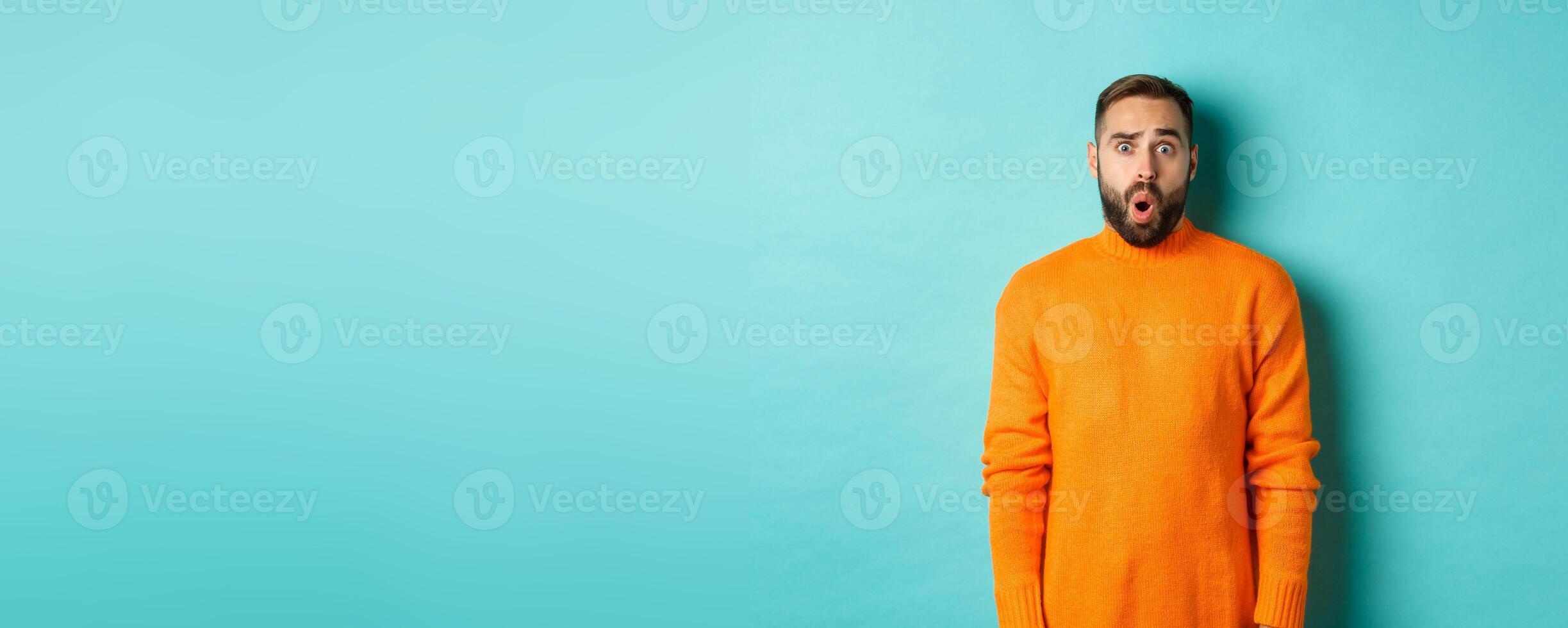 Shocked and confused man looking in awe at promo offer, standing near copy space on turquoise background photo