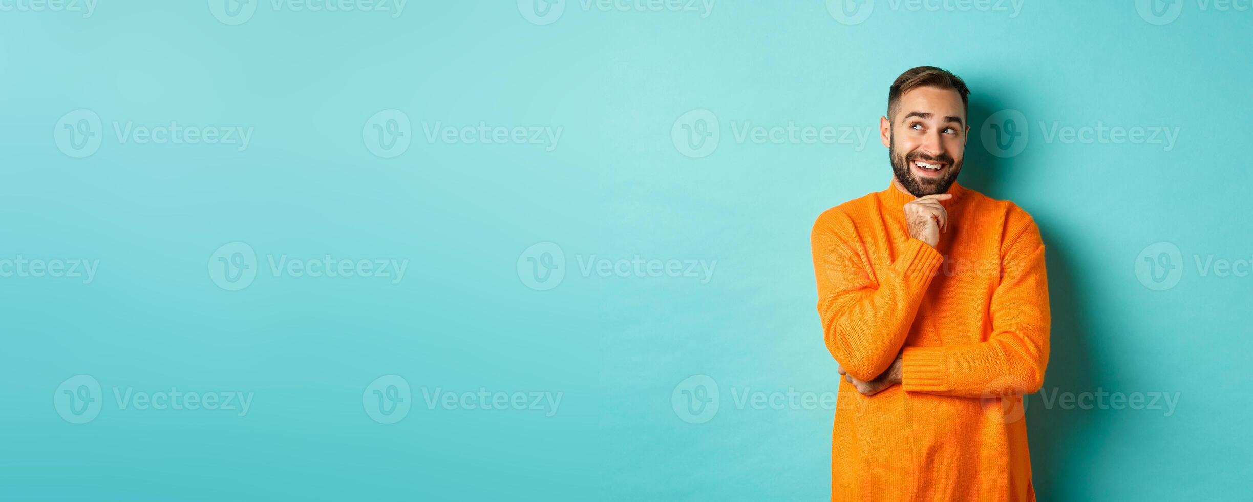 Thoughtful bearded guy making choice, shopping and looking at upper left corner, smiling satisfied, standing over turquoise background photo