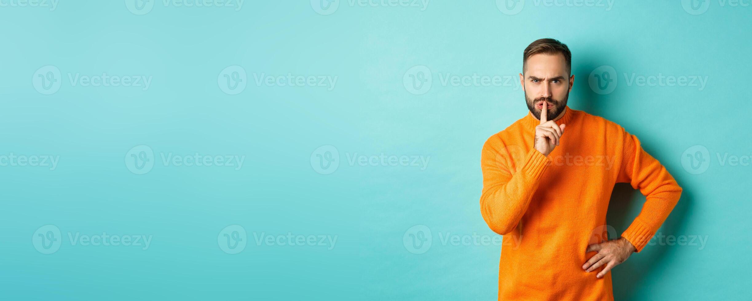 Angry bearded guy telling be quiet, hushing and frowning displeased, shut up gesture, standing over turquoise background photo