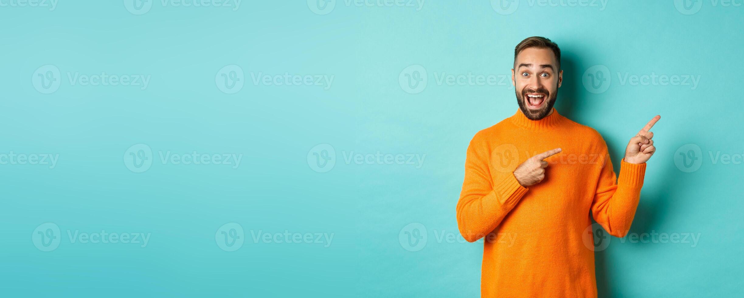 Excited man making an announcement, pointing fingers right your logo, standing over turquoise background photo