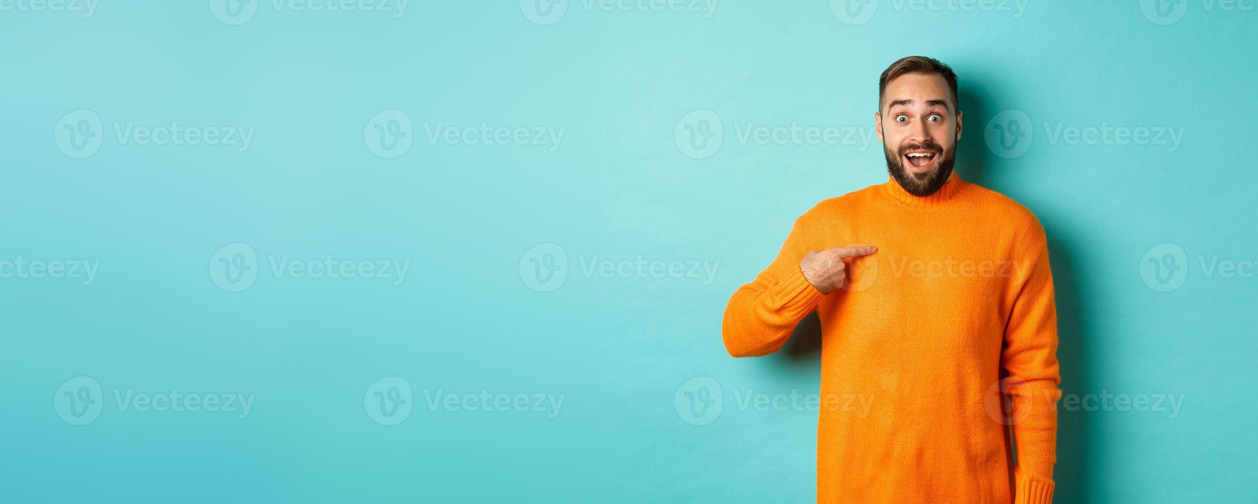 Excited man pointing at himself, looking amazed and happy, being chosen, standing over light blue background photo