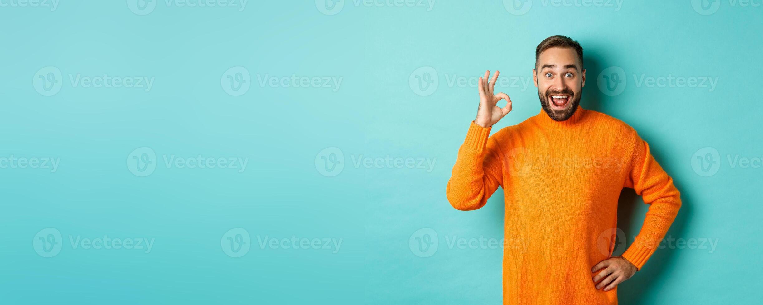 Impressed man recommending promo, showing okay sign and smiling amazed, approve and agree, standing over light blue background photo