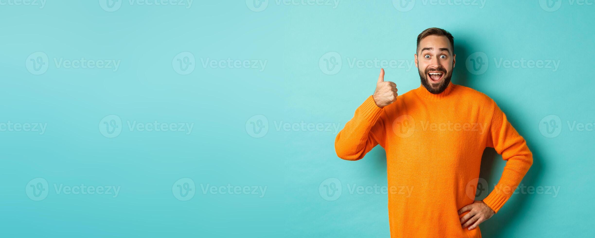 Well done. Handsome bearded man showing thumb up, praising good work, recommend excellent product, like and approve, smiling satisfied, standing over light blue background photo