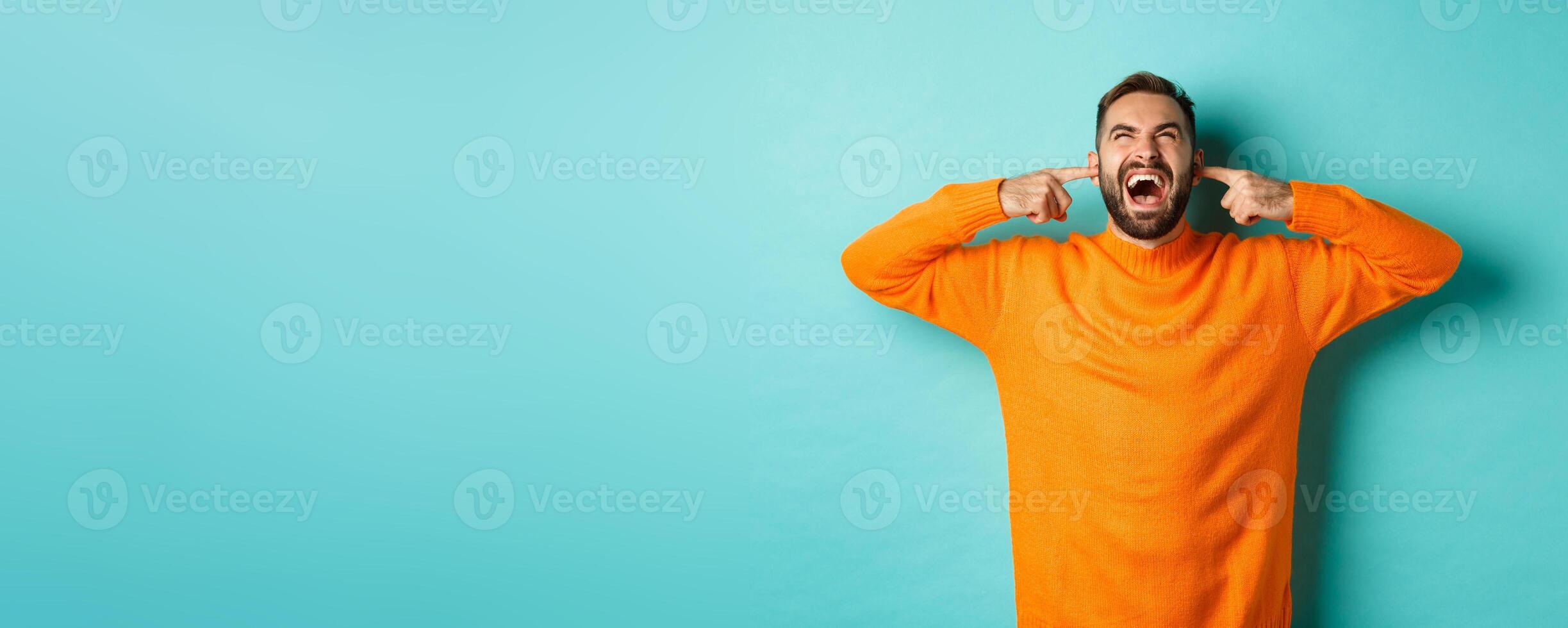 Frustrated and annoyed man shouting at neighbours upstairs, shut ears with fingers, loud bothering noise, standing over light blue background photo