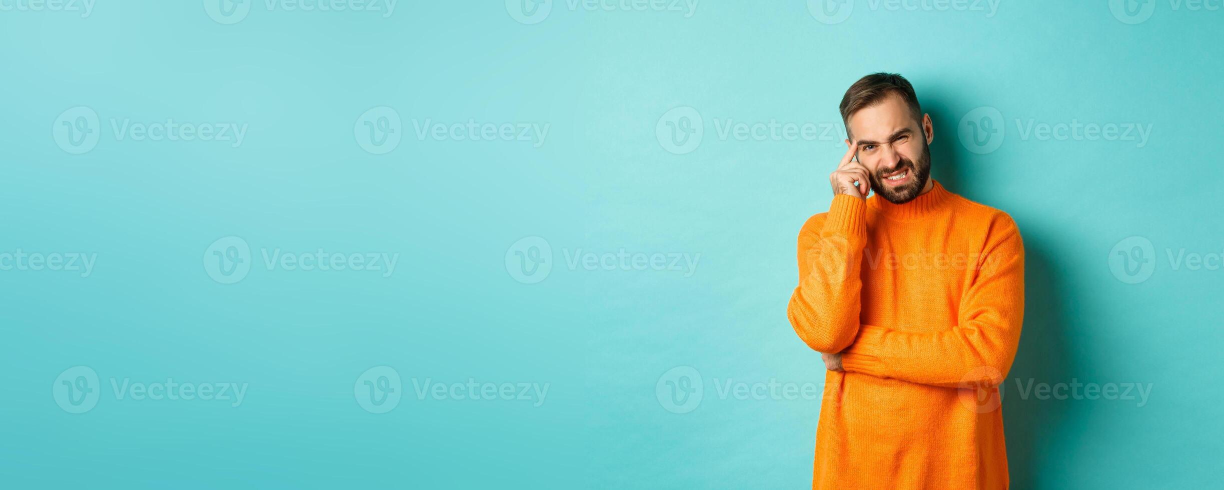 Man with beard, grimacing and cringe from something embarrassing, looking with awkward face, standing over light blue background photo