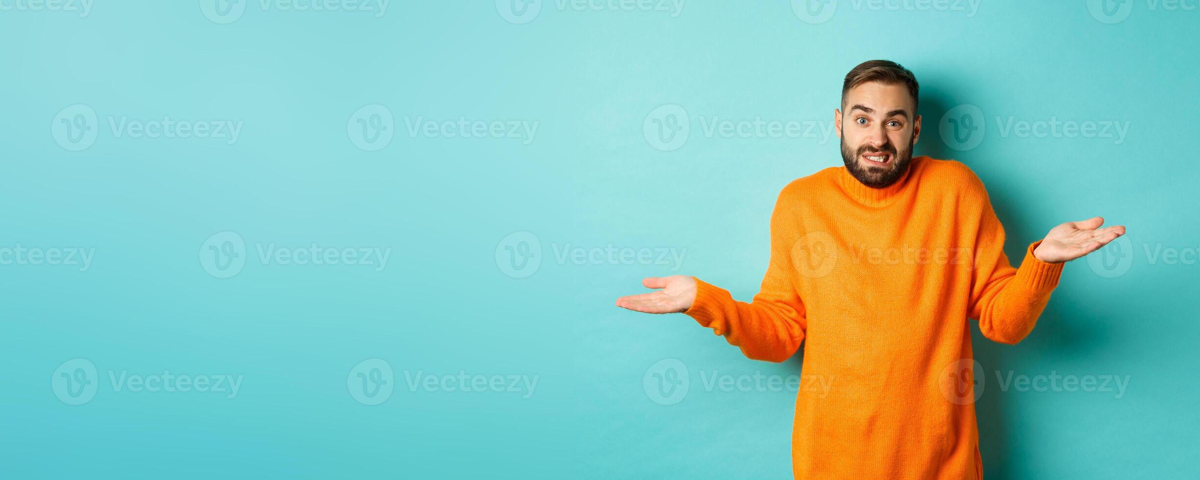 Confused caucasian man with beard, shrugging and looking clueless, standing indecisive against turquoise background photo