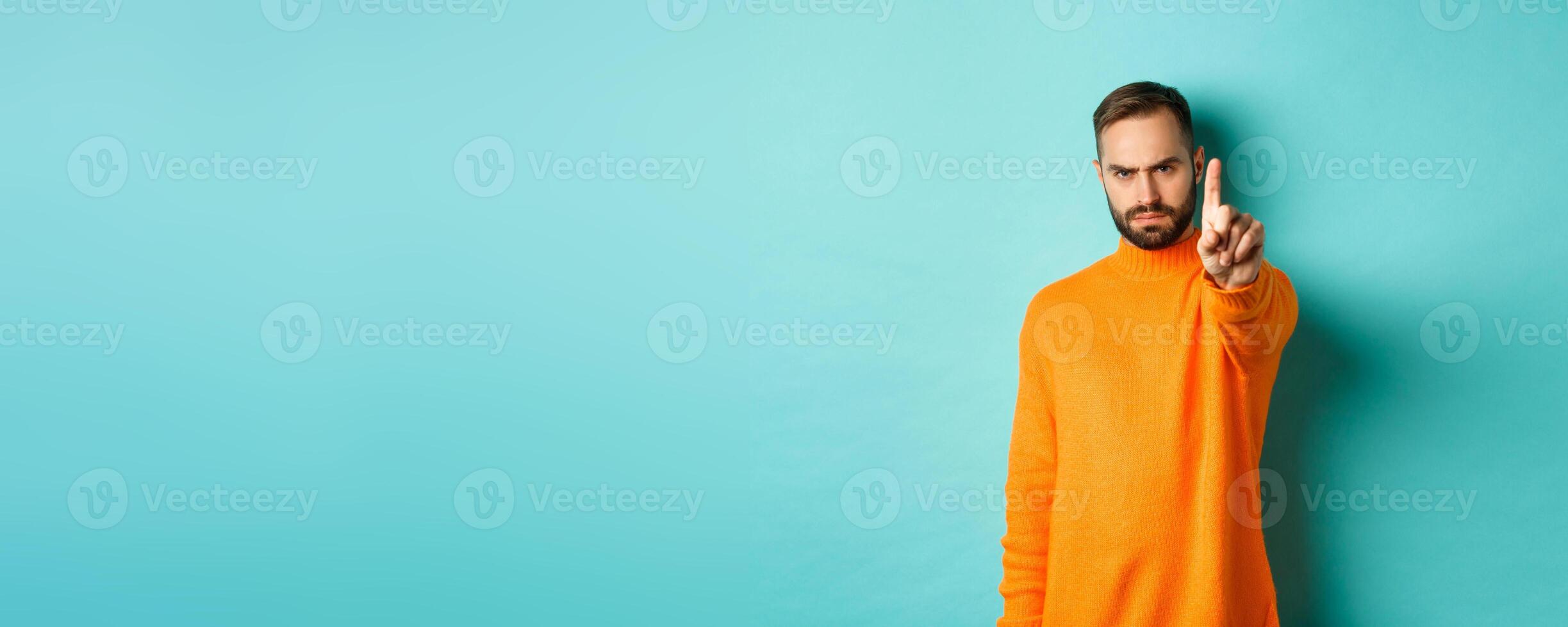 Serious bearded man frowning, shaking finger to prohibit action, forbid something, express disappointment, disagree with you, standing over light blue background photo