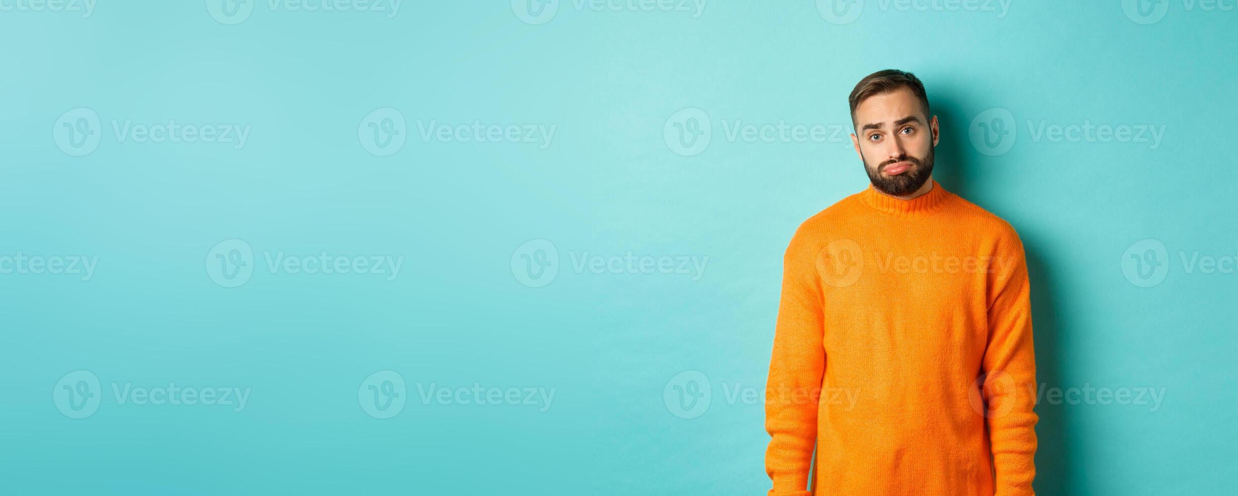 Sad man looking at camera, sulking and feeling distressed, standing over light blue background photo