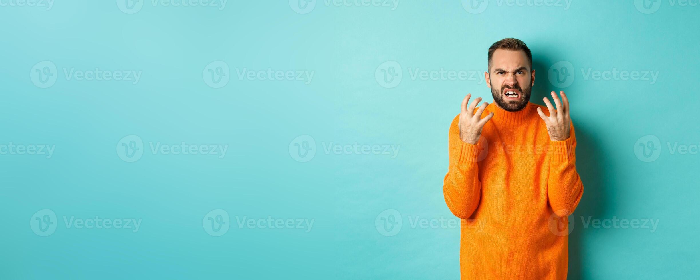 Image of angry man looking disappointed and mad, shaking hands and grimacing with disdain, standing distressed against light blue background photo