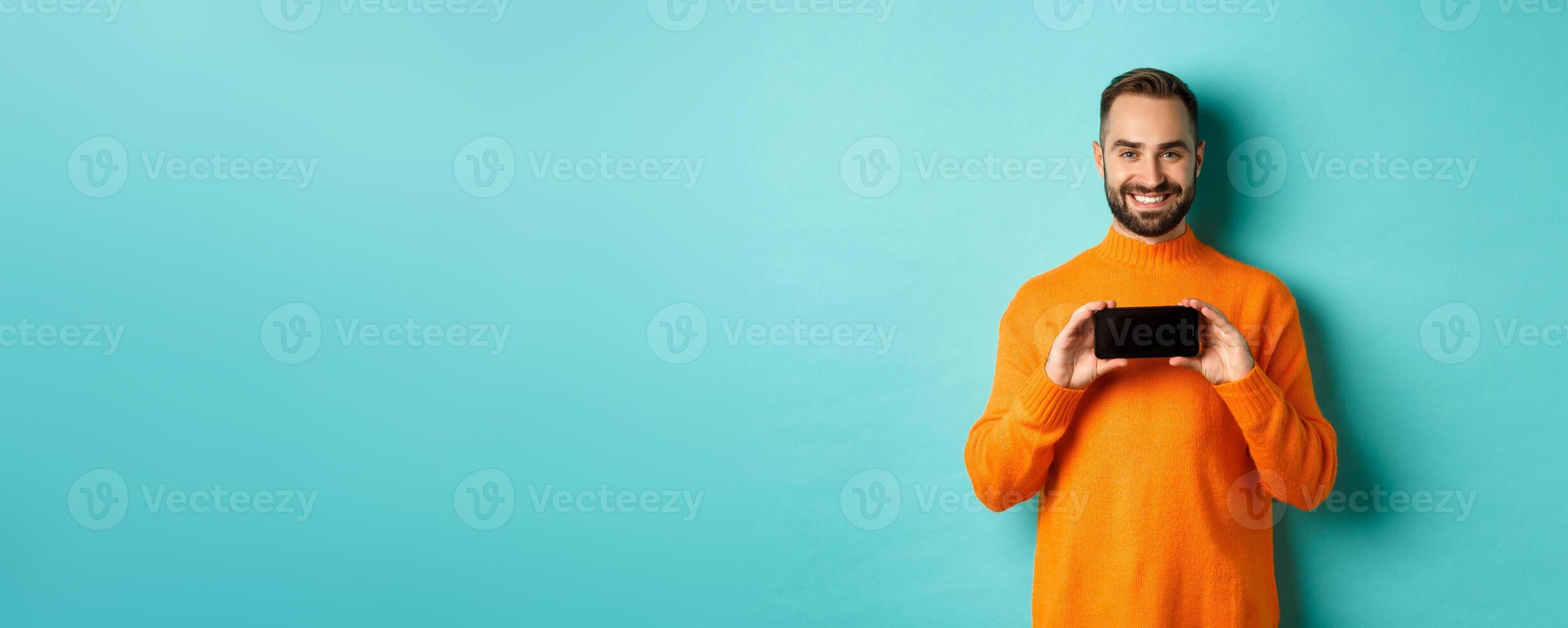 Handsome bearded adult man showing mobile screen, holding smartphone horizontally, concept of applications and online shopping photo