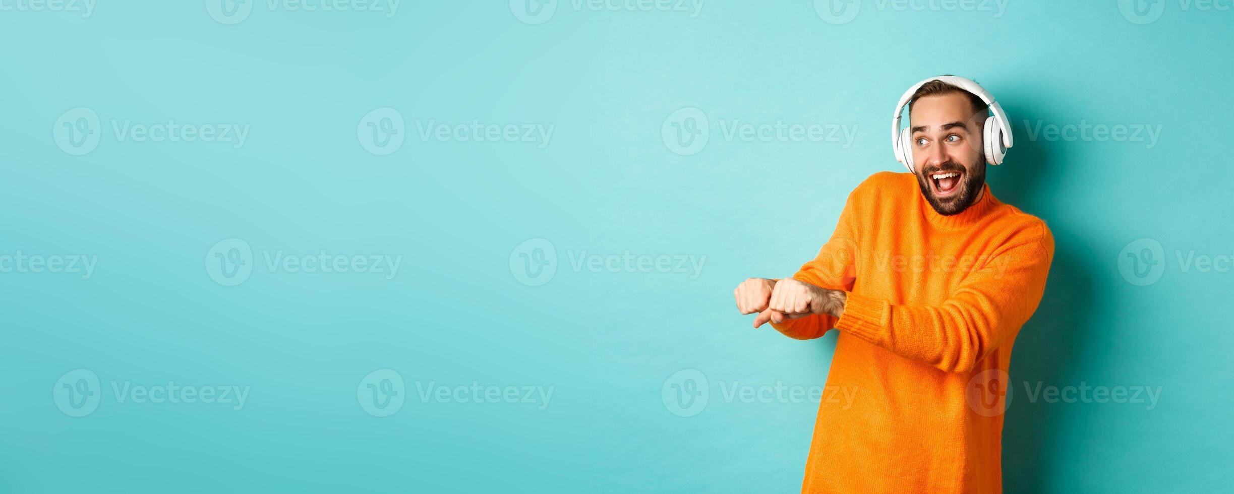 Happy man listening music in headphones and dancing funny, standing over turquoise background photo
