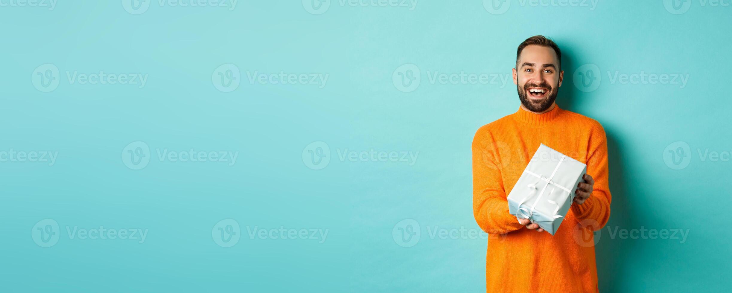 Holidays and celebration concept. Cheerful bearded man giving present, holding gift and smiling, congratulating you, standing over turquoise background photo
