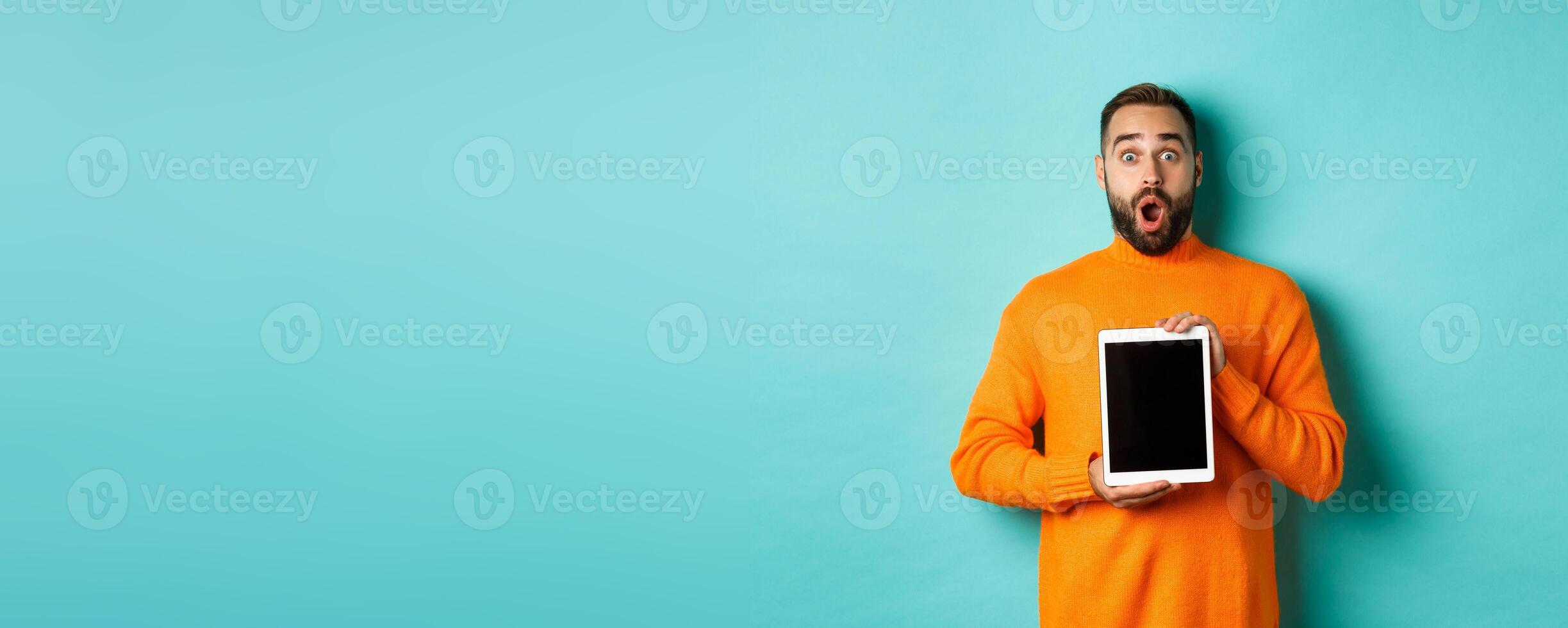 Technology. Surprised bearded man drop jaw, staring at camera and showing digital tablet screen, standing againt light blue background photo