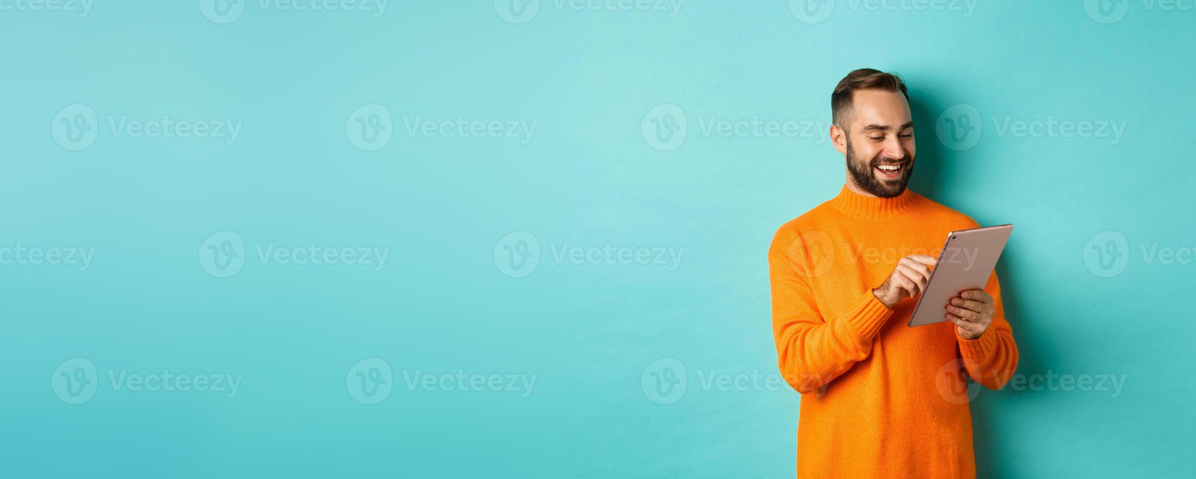 Handsome adult man working on digital tablet and smiling, shopping online, standing over light blue background photo