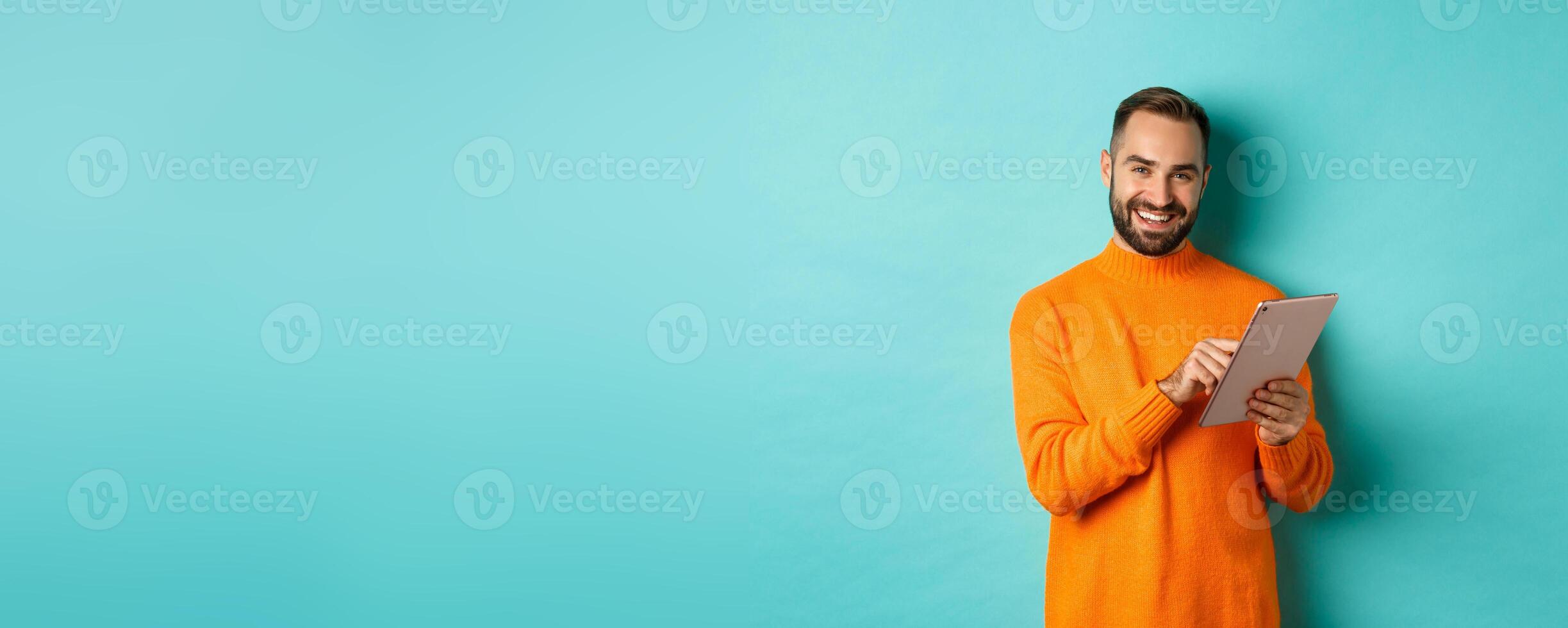 Handsome adult man using digital tablet and smiling, shopping online, standing over light blue background photo