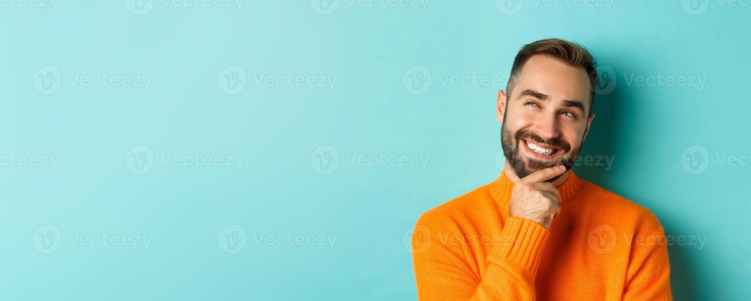 Close-up of caucasian male model having an idea, smiling and looking upper left corner thoughtful, imaging plan, standing over light blue background photo