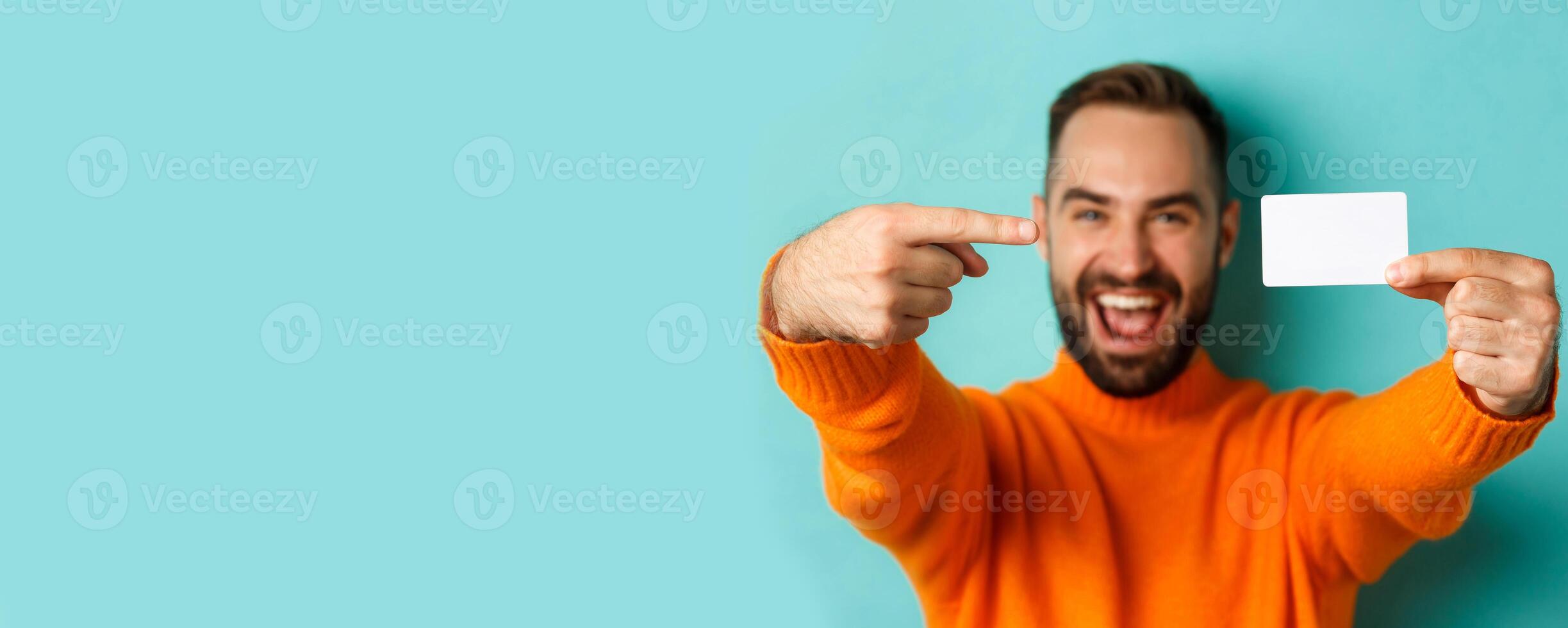 Close-up of handsome caucasian man going on shopping, showing credit card and smiling, standing over turquoise background photo