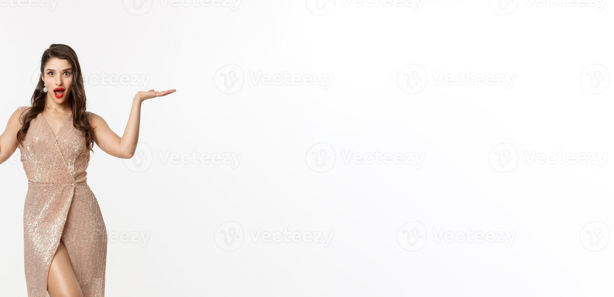 Christmas party and celebration concept. Attractive brunette female model in elegant dress, showing two offers, raising hands and holding something on copy space, white background photo