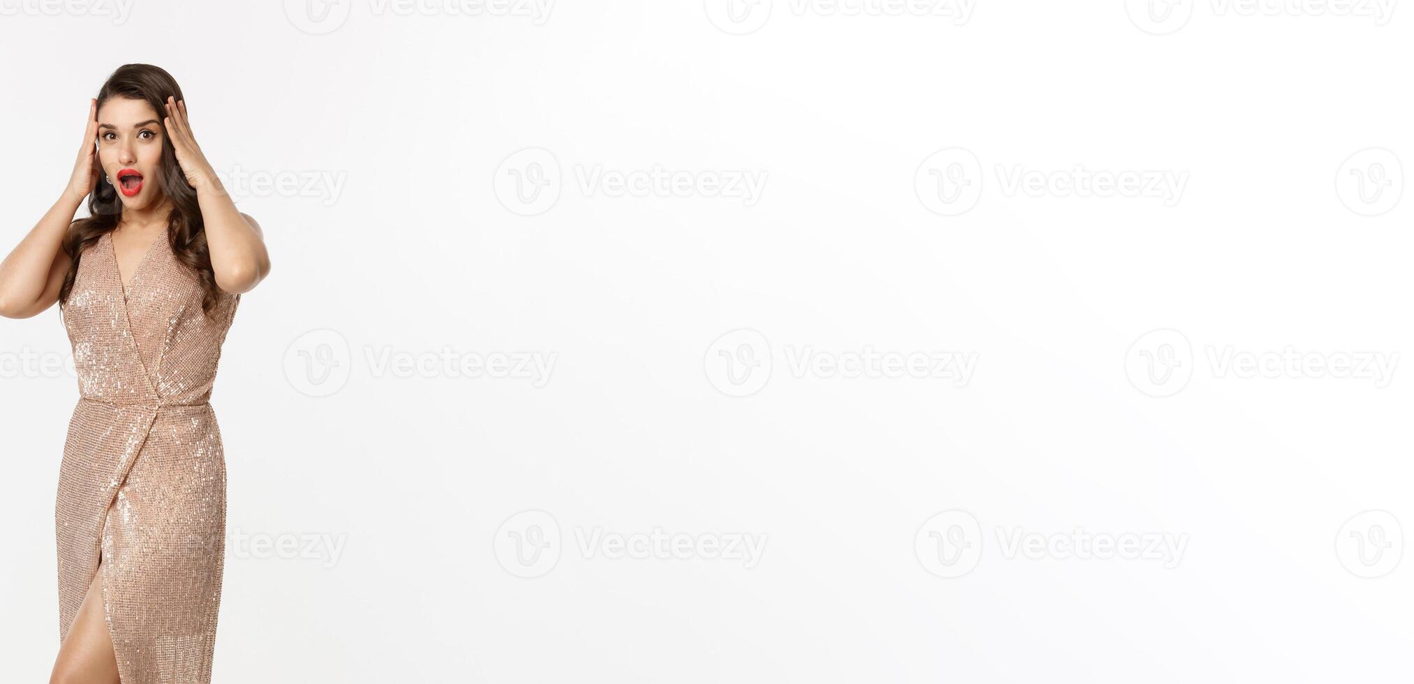 Christmas party and celebration concept. Full length of beautiful brunette woman looking surprised, wearing elegant dressed and staring with disbelief at camera, white background photo