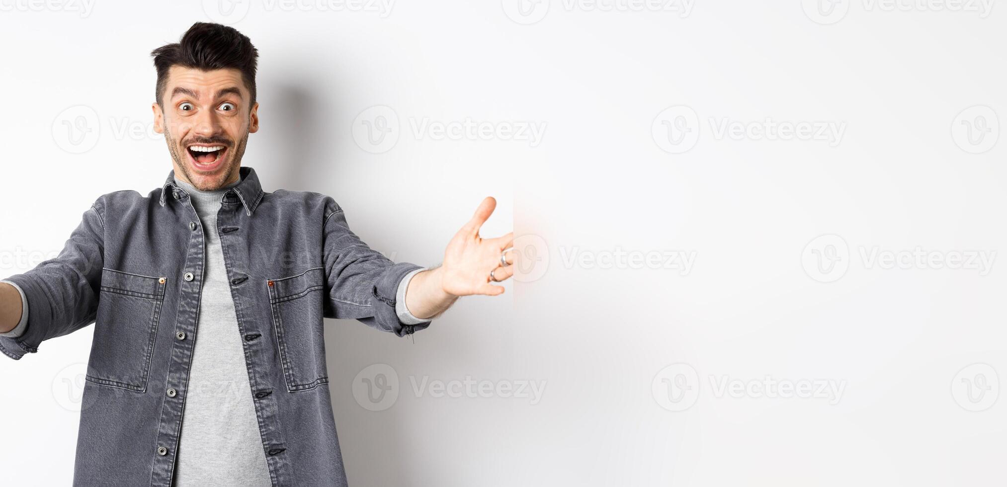 Excited young man stretch out hands for hug, cuddling you, welcoming guest and smiling, inviting people, standing on white background photo