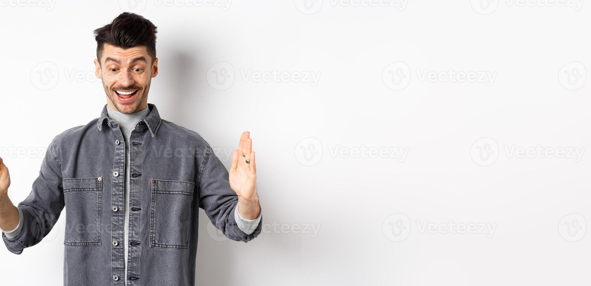 Excited caucasian man showing big size object, shaping large thing and smiling amazed, standing on white background photo