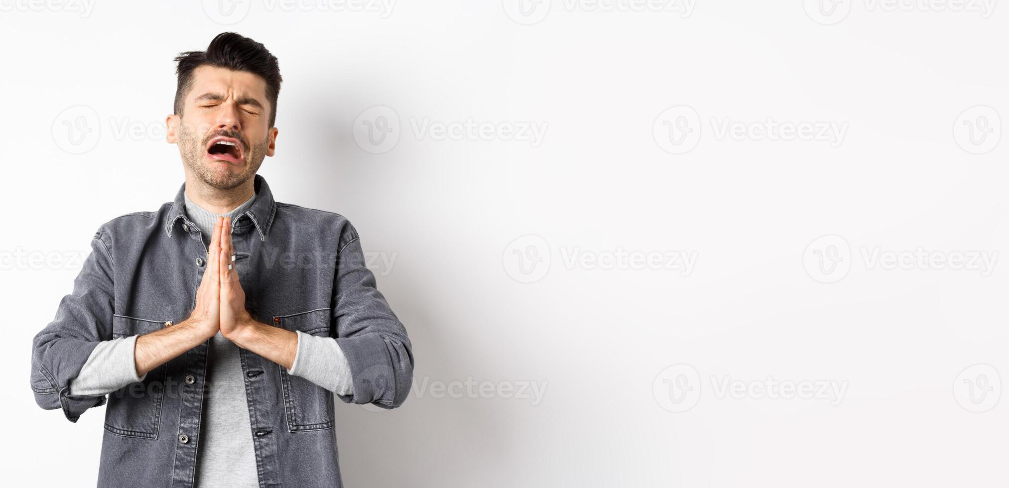 Miserable man begging for help, need something and crying, pleading with sad face, standing on white background desperate photo