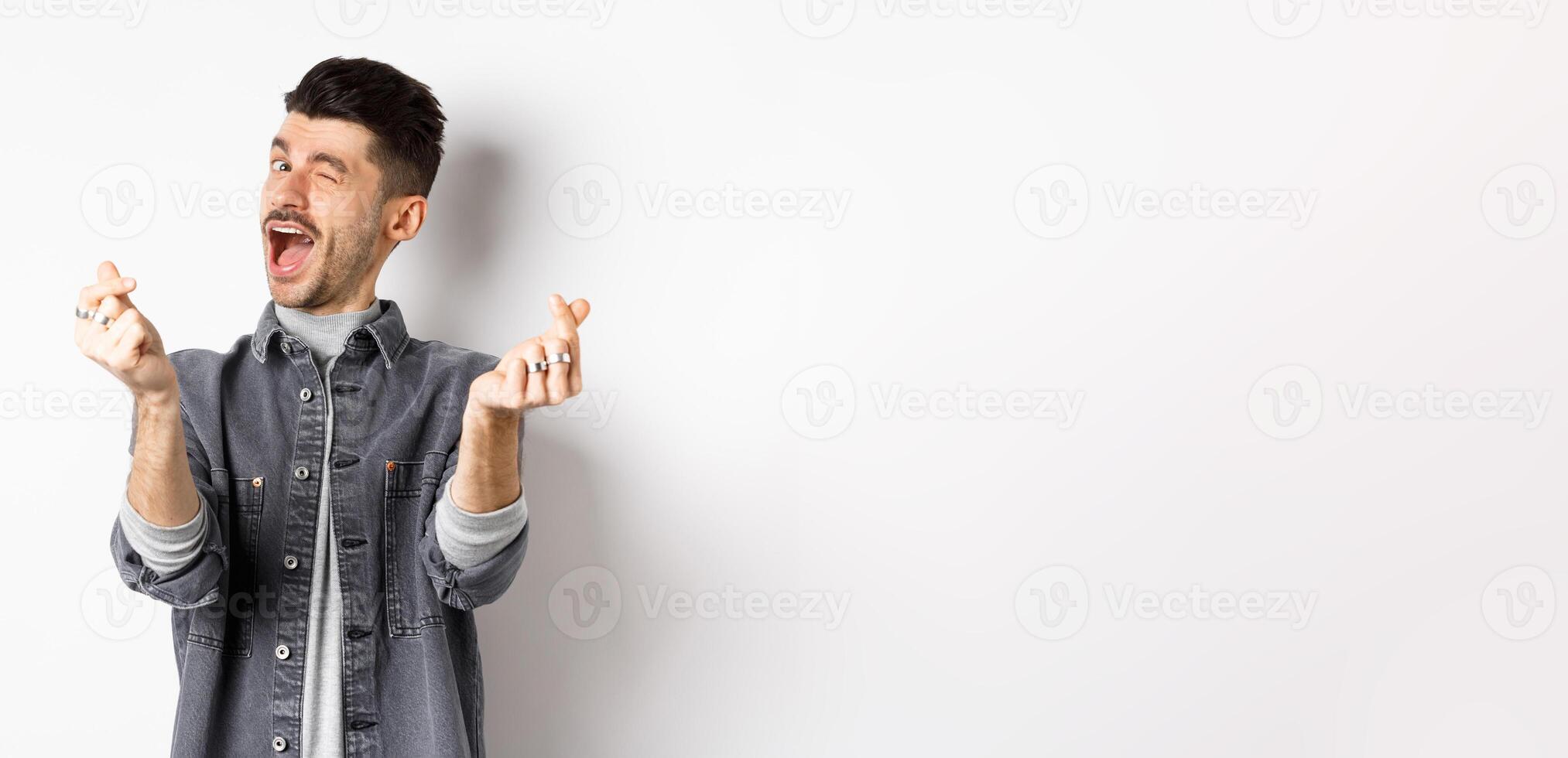 Funny guy winking and showing hand hearts sign, feeling romantic and happy, standing on white background photo