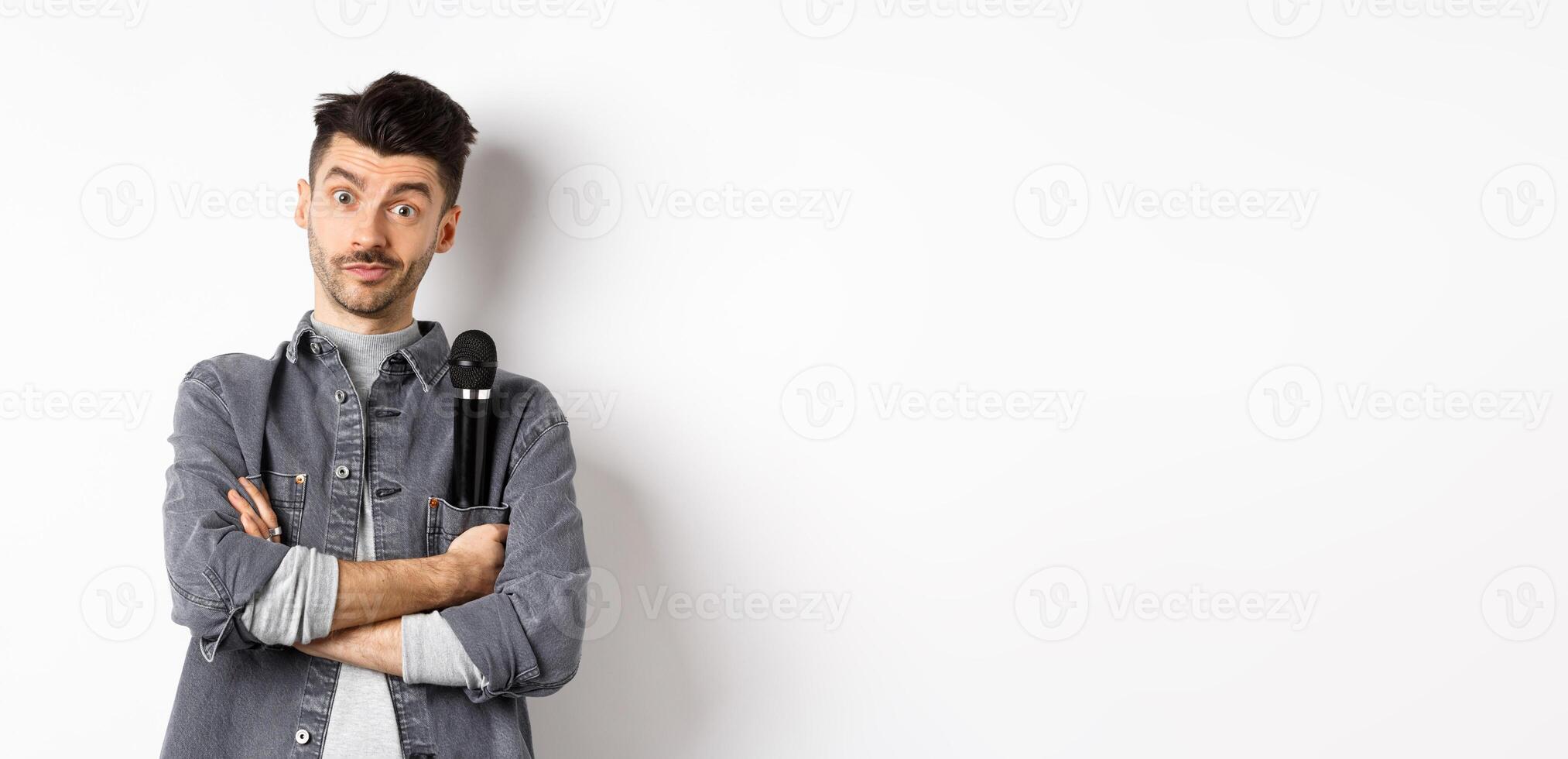 Image of funny male entertainer or singer, holding microphone in pocket of jacket and look at camera with arms crossed, standing against white background photo
