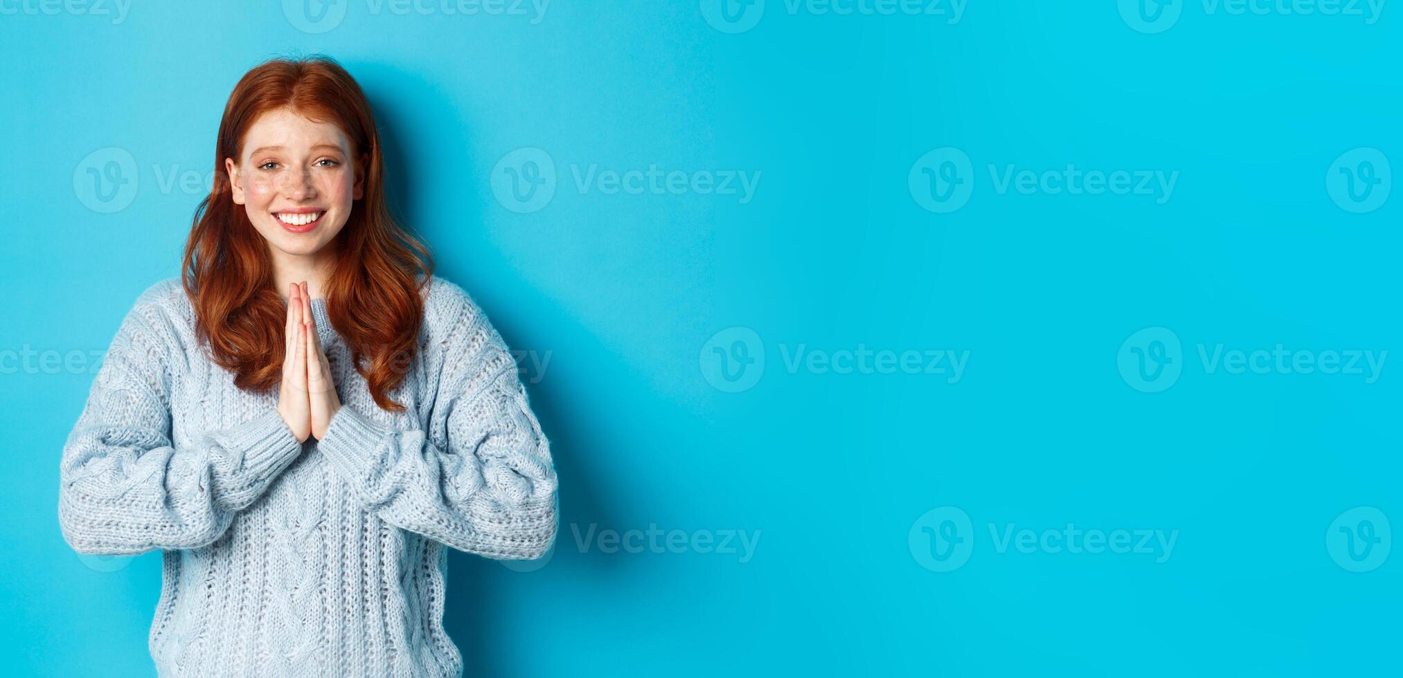 Cute redhead girl saying thank you, smiling and looking at camera, expressing gratitude, standing against blue background photo