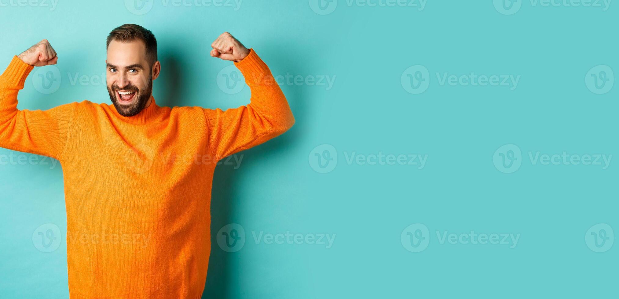 Young and strong man looking confident, flex biceps and show-off muscle strengths, smiling self-assured, standing over light blue background photo