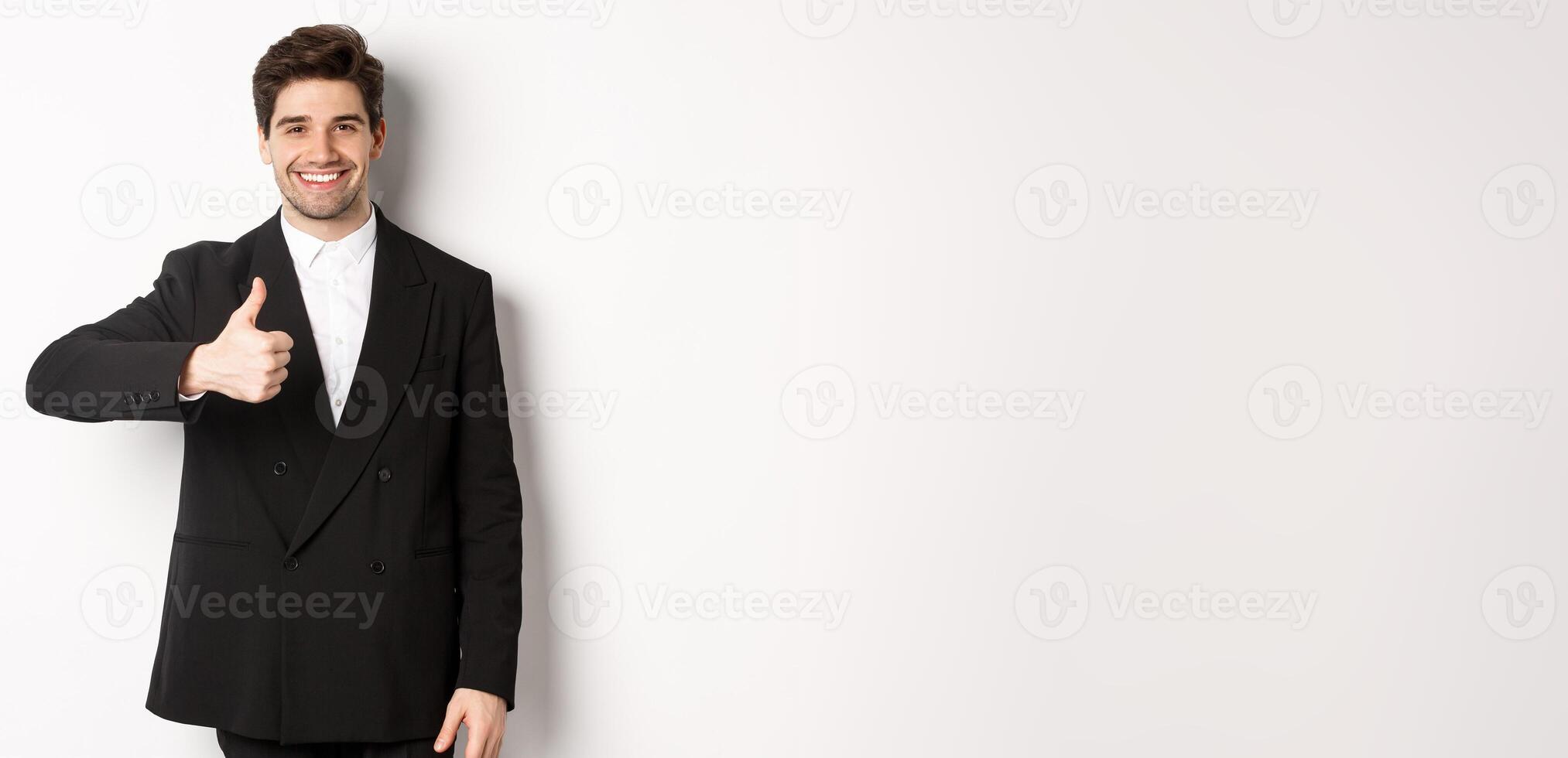 Portrait of handsome and confident male realtor, showing thumb-up and smiling, guarantee quality and recommending company, standing over white background photo