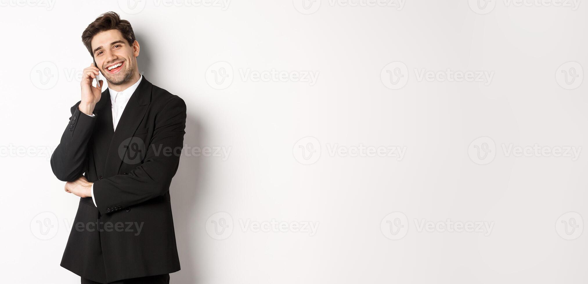 Image of handsome, successful businessman talking on phone, smiling pleased, standing in suit against white background photo