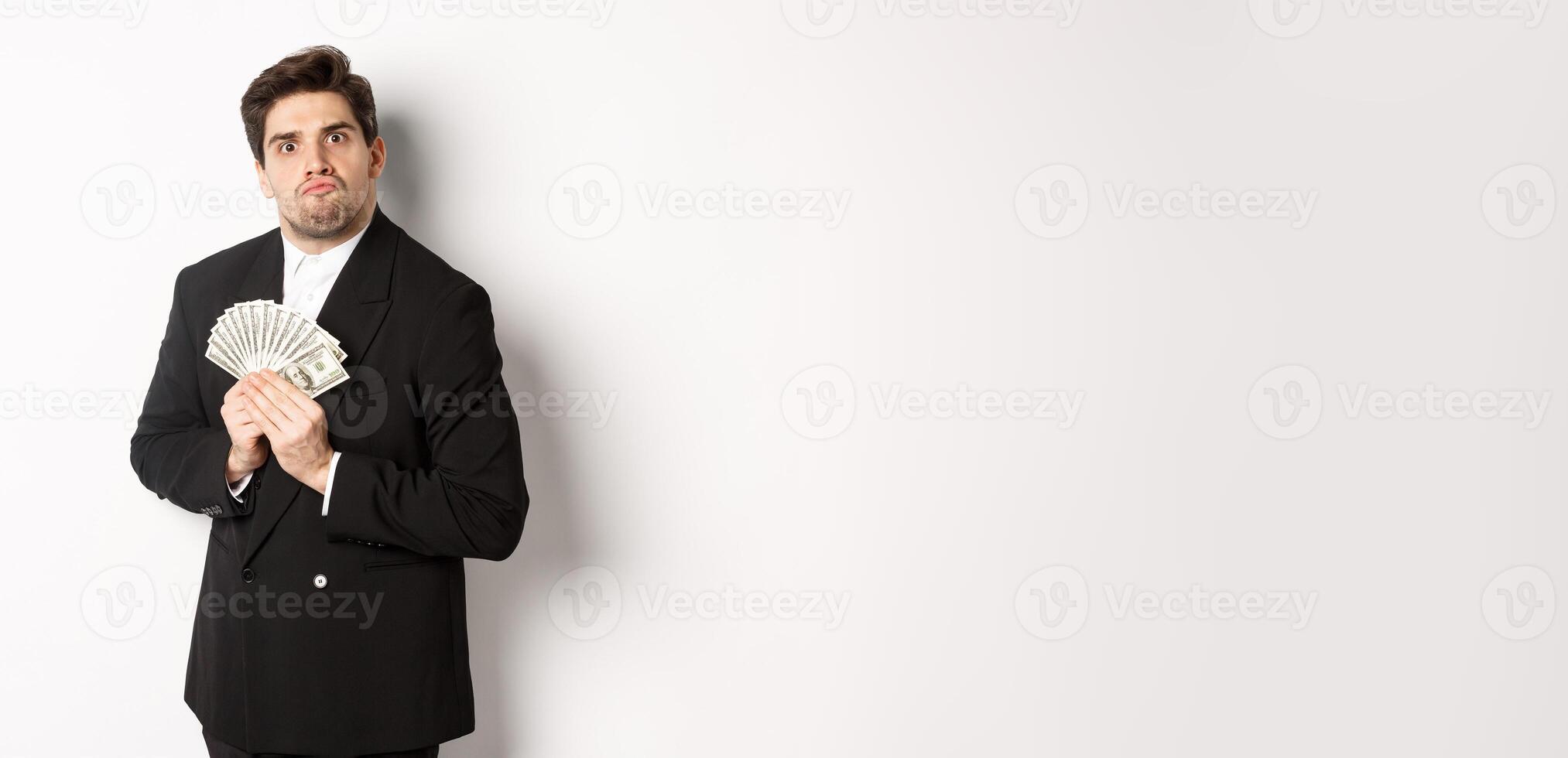 Image of greedy guy in black suit, holding money and unwilling to share, standing over white background photo