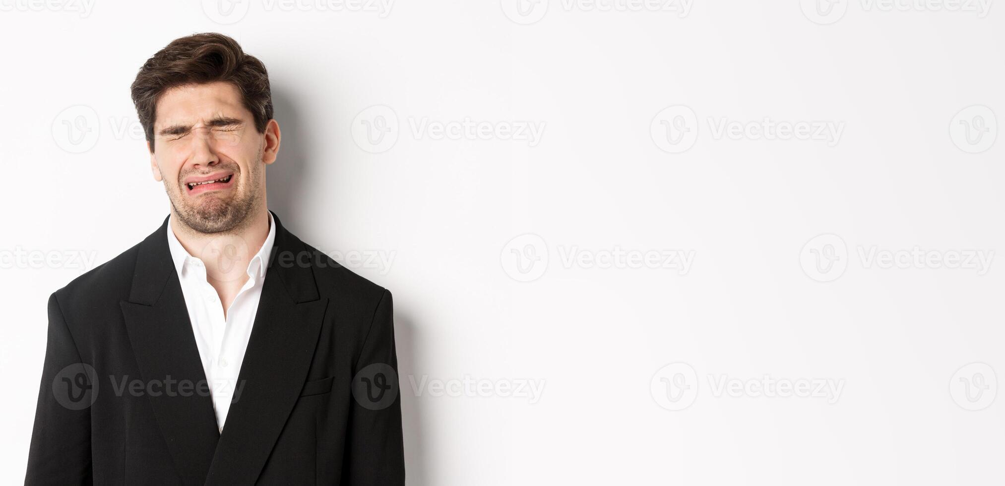 Close-up of miserable man in suit, crying and sobbing, feeling sad, standing against white background photo