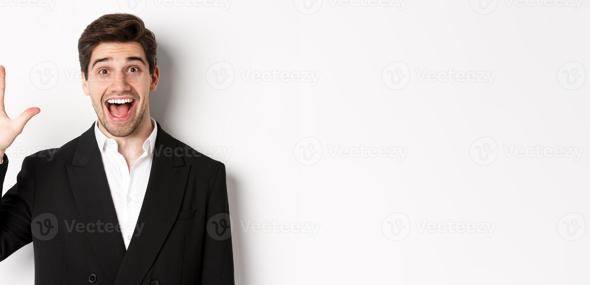 Close-up of handsome businessman in black suit, smiling amazed, showing number five, standing over white background photo