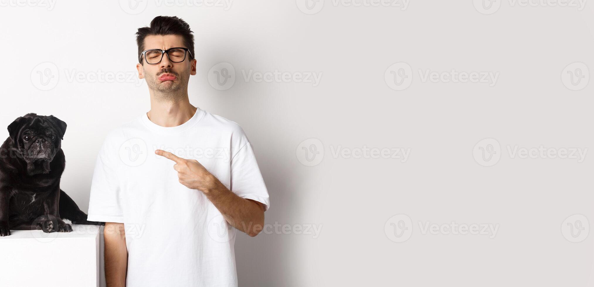 Sad and gloomy pet owner pointing at his black pug dog and sobbing, standing upster against white background photo